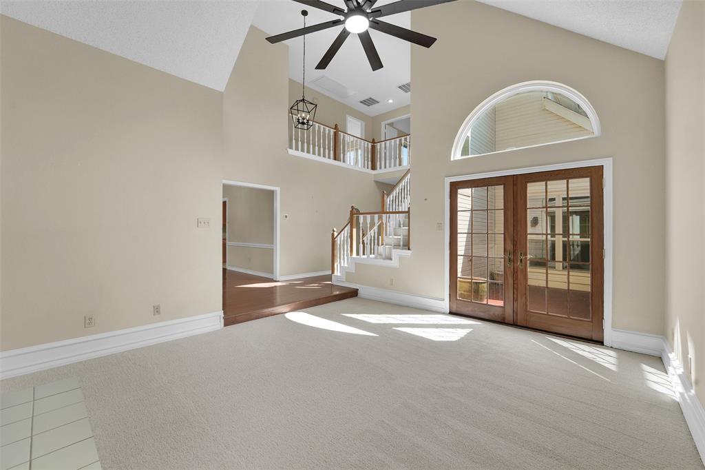 Vaulted ceilings featuring a multi-blade ceiling fan, arched window, French glass doors, and a wood-railing staircase with balusters