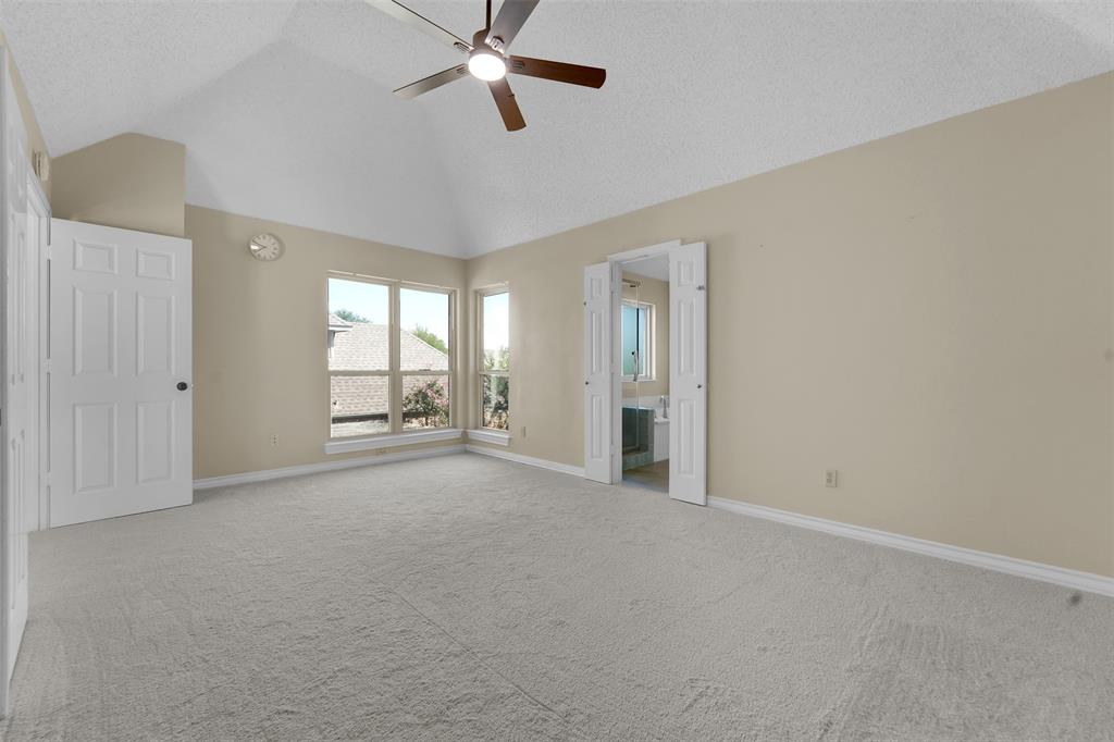 Vaulted ceiling featuring a ceiling fan with light fixture, neutral wall finishes, and multiple windows providing natural light