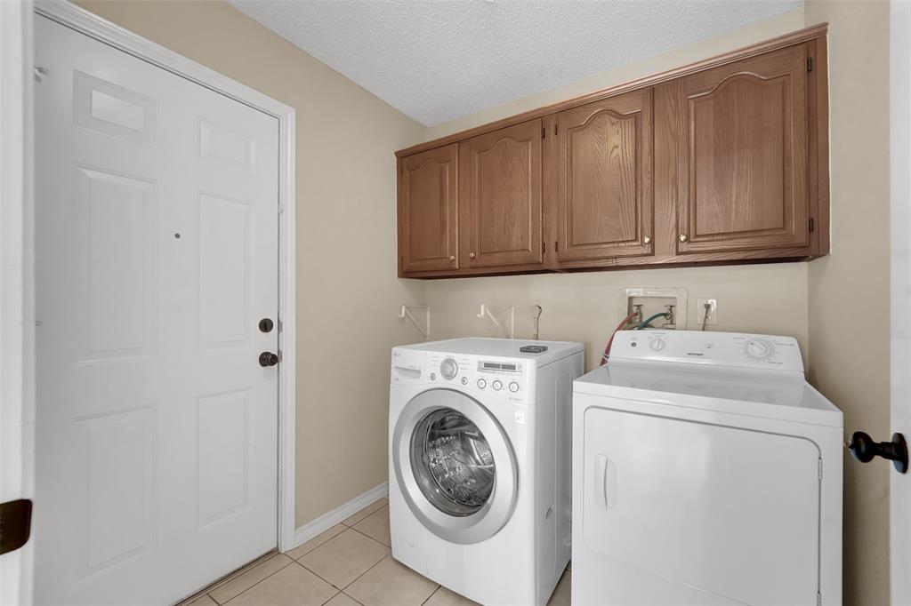 Utility room featuring tile flooring, wood-finish wall-mounted cabinetry, and dedicated laundry hookups