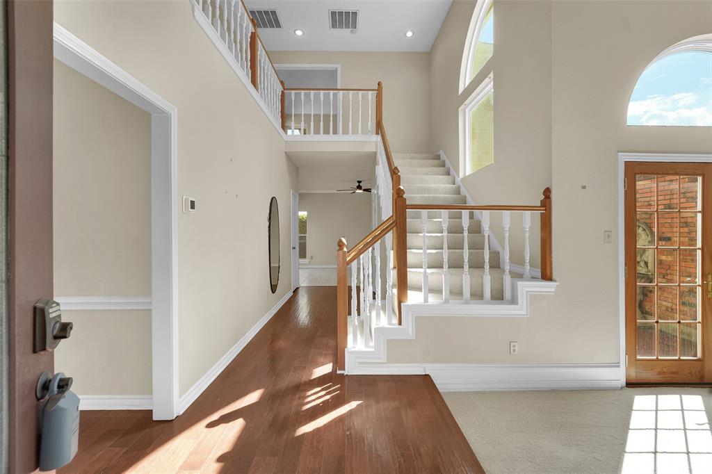 Foyer featuring high ceilings, hardwood flooring, a staircase with a white balustrade and wood handrail, and arched windows