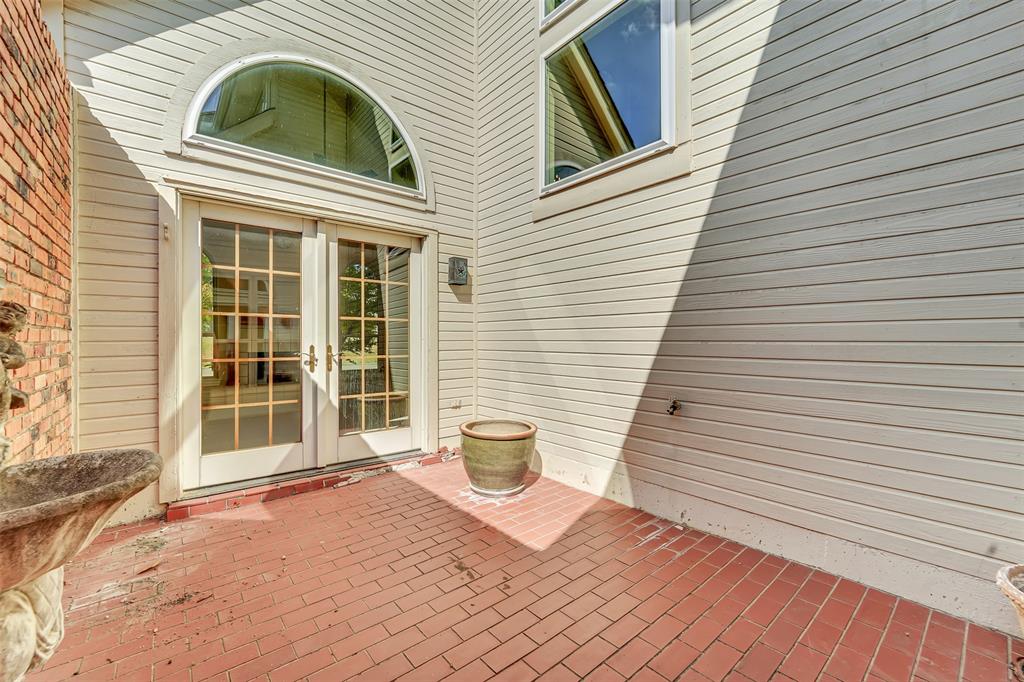 Brick-paved patio featuring horizontal lap siding, double French doors, a semi-circular transom window, and stone masonry accent wall