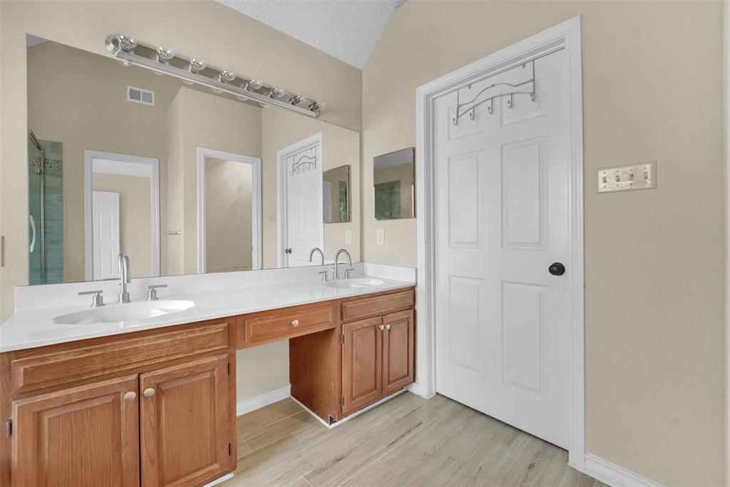 Dual-sink vanity with wood-finish cabinetry, solid surface countertop, wall-to-wall mirror, and overhead light fixture