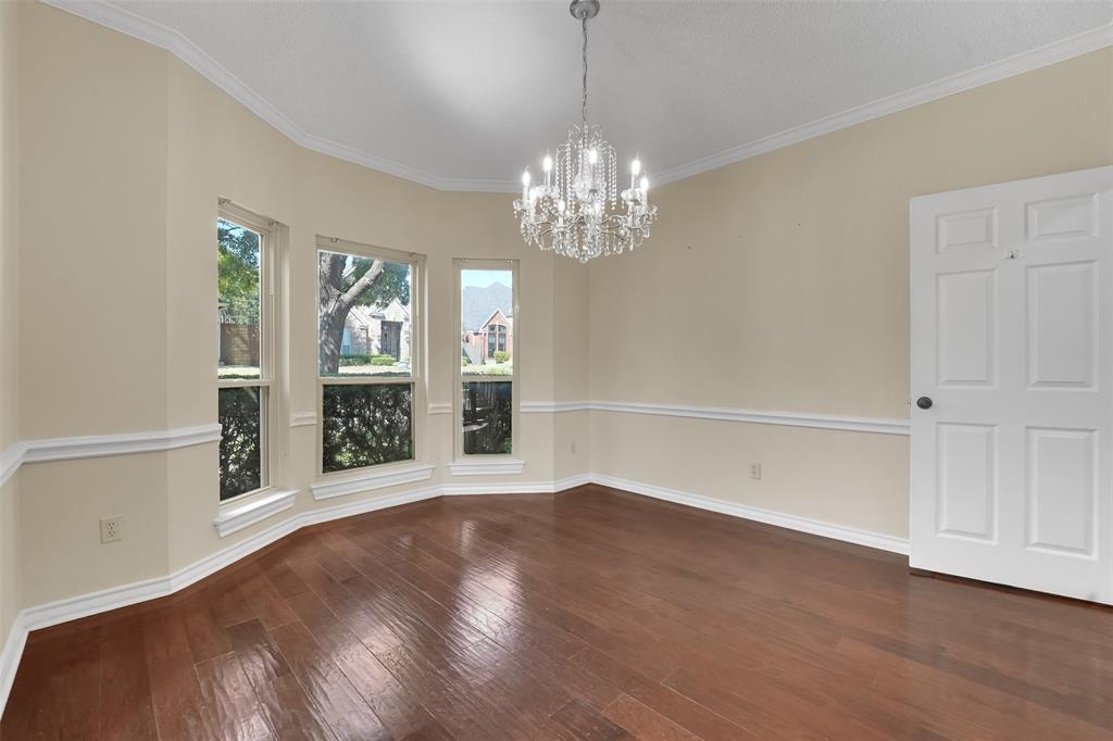 Bay window with natural lighting, wood-finish flooring, crown molding, chair rail molding, and crystal chandelier