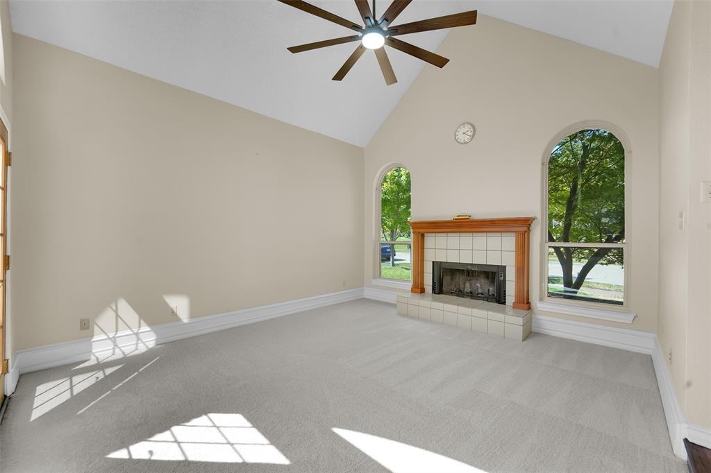 Vaulted ceiling featuring a central multi-blade ceiling fan, arched windows, and a masonry fireplace with a wood mantel and tile hearth