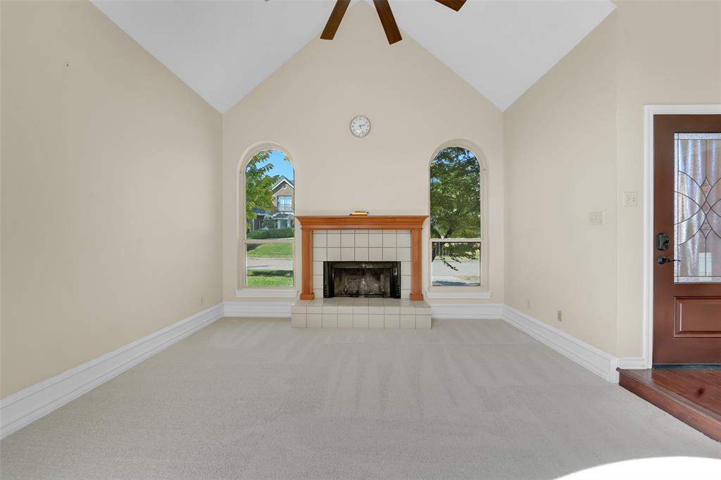 Vaulted ceiling featuring a central ceiling fan, fireplace with a wood mantel and tile surround, and arched windows