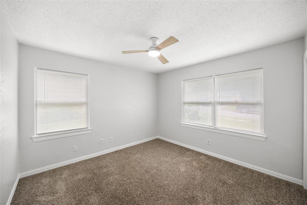 Carpeted room featuring multiple windows with blinds, a ceiling fan with light fixture, and textured walls with baseboards