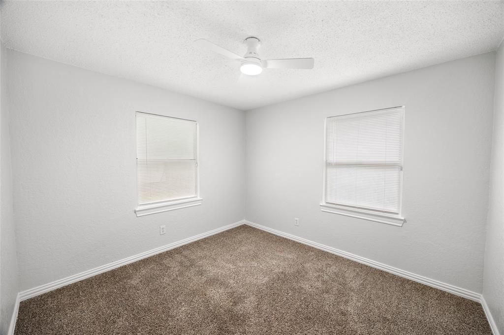 Room featuring light grey walls, brown carpet, two windows with blinds, white trim, and a white ceiling fan
