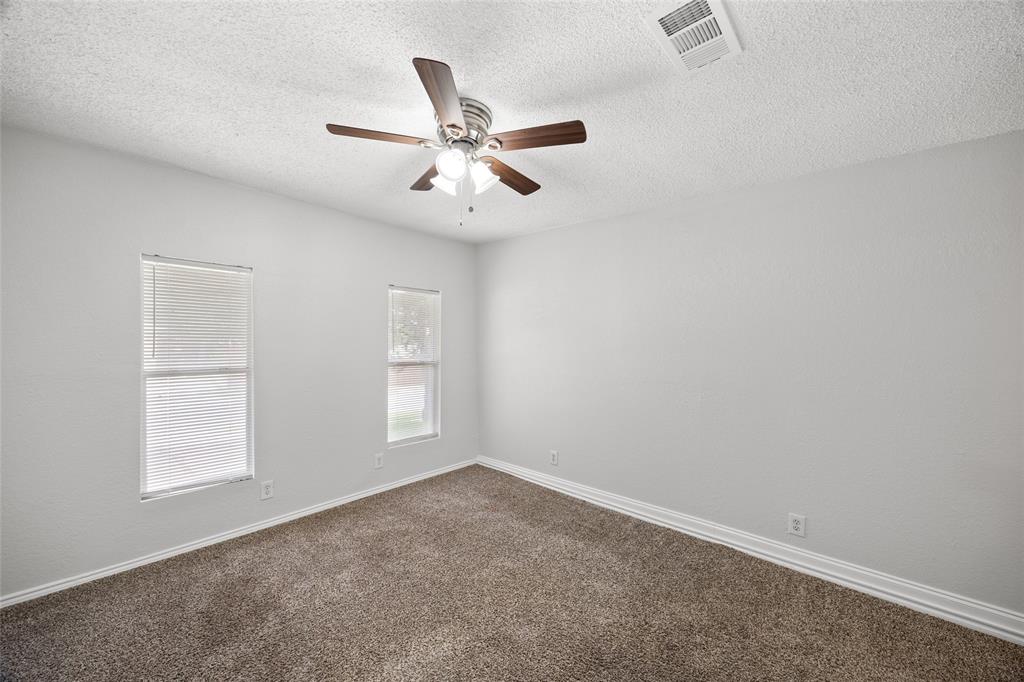 Spacious room featuring neutral carpeting, light gray walls, a textured ceiling, two windows with blinds, and a ceiling fan with integrated lighting
