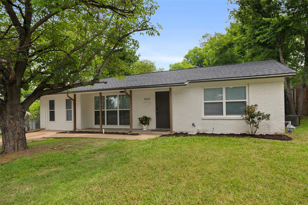 White brick exterior with a dark shingle roof and a spacious front yard