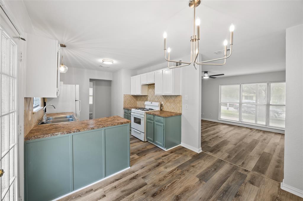 Open-concept kitchen featuring white upper cabinetry, sage green lower cabinetry, wood-finish flooring, and a contemporary chandelier