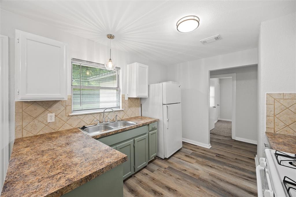 Kitchen featuring wood-finish flooring, white upper cabinetry, sage green lower cabinetry, and a tile backsplash