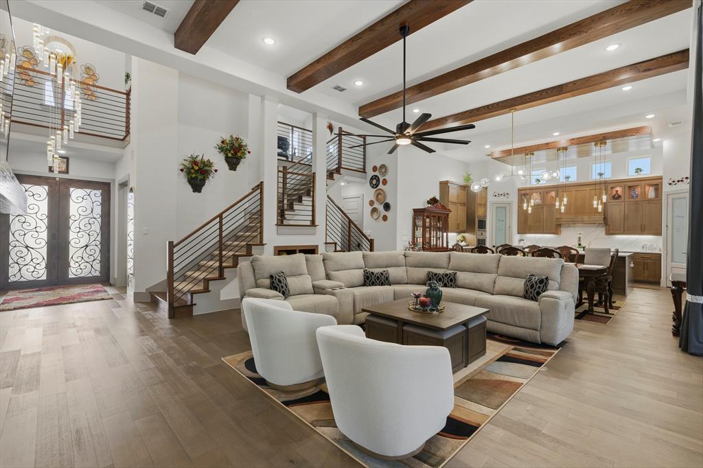 Open-concept interior featuring exposed wooden ceiling beams, wood-finish flooring, metal staircase railings, ornate iron double front doors, and custom wooden cabinetry