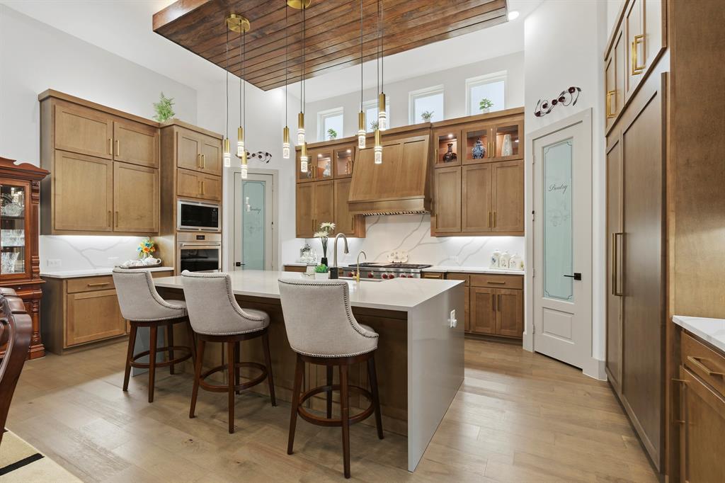 Kitchen featuring floor-to-ceiling wood cabinetry, a center island with a waterfall countertop, suspended pendant lighting, wood-finish flooring, and a recessed ceiling panel with wood cladding
