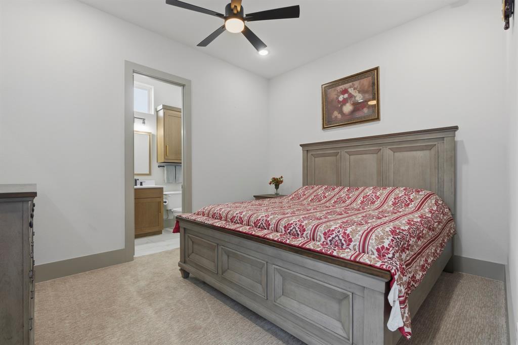 Neutral interior room featuring neutral carpeting, a ceiling fan with integrated lighting, and a doorway opening to a secondary space with a wood-finish vanity and cabinetry