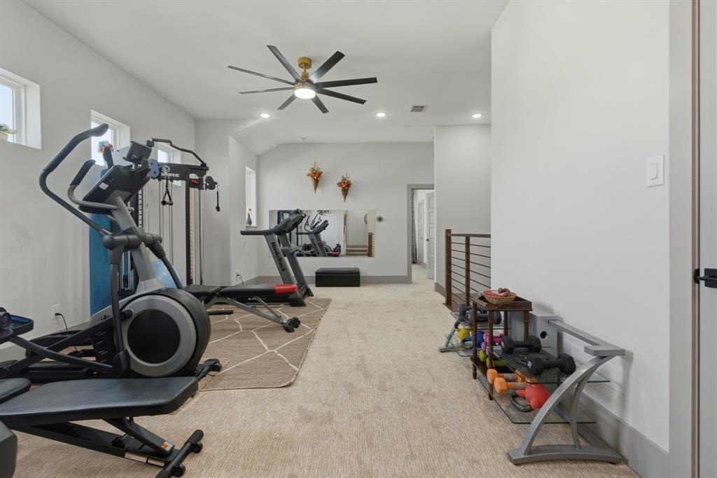 Multi-purpose room featuring neutral carpeting, a large wall-mounted mirror, recessed lighting, a multi-blade ceiling fan, and metal-railing staircase accents