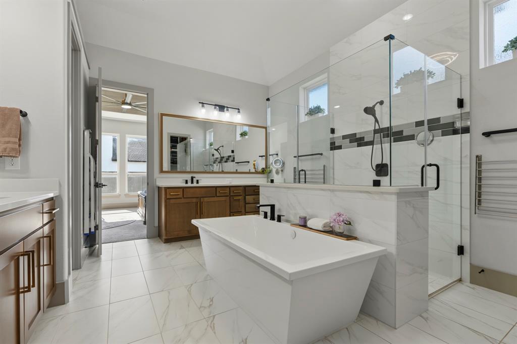 Freestanding soaking tub, walk-in glass-enclosed shower with tile surround, wood-finish cabinetry, tile flooring, and wall-mounted vanity lighting