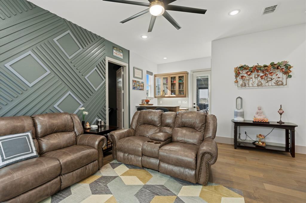 Feature wall with geometric millwork, wood-finish flooring, recessed lighting, ceiling fan with light kit, and built-in glass-front cabinetry