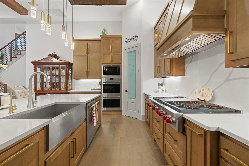 Gourmet kitchen featuring custom wood cabinetry, quartz countertops, stainless steel farmhouse sink, professional-grade gas range with integrated vent hood, and multi-light pendant fixtures
