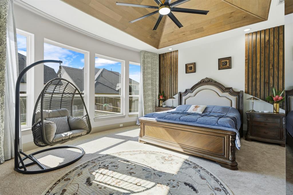 Vaulted wood-plank ceiling featuring a multi-blade ceiling fan, large windows, and decorative vertical wood wall paneling