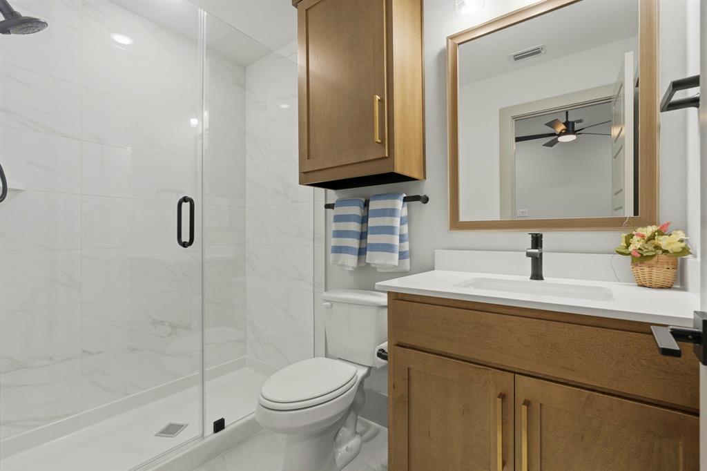 Bathroom featuring a walk-in shower with glass enclosure, white stone-finish wall tile, wood-finish cabinetry, quartz countertop, and framed mirror