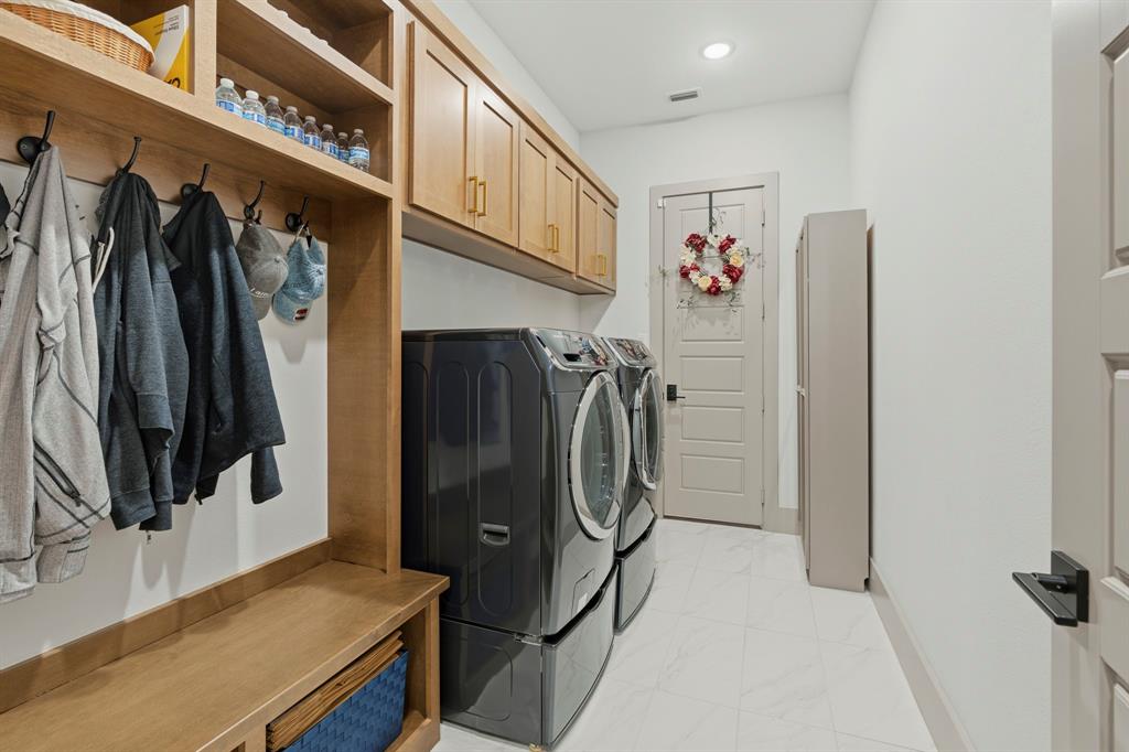 Utility room featuring custom wood cabinetry, integrated mudroom storage with coat hooks, tile flooring, and a solid-core interior door with matte black hardware