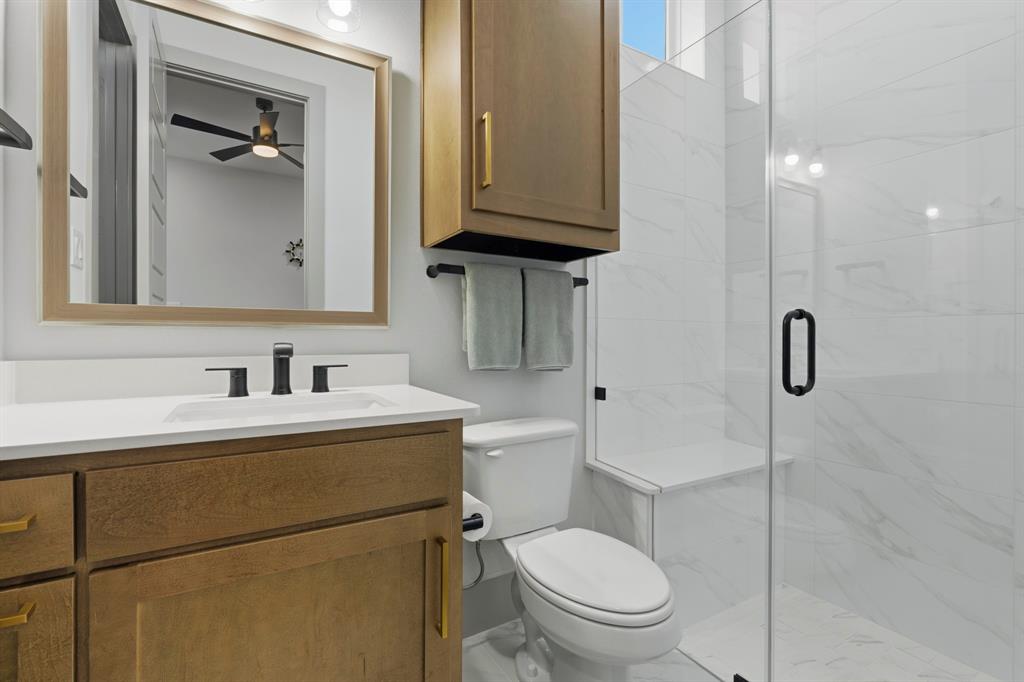 Bathroom featuring a wood-finish vanity with a white countertop, wall-mounted cabinetry, a glass-enclosed shower with tiled walls and a built-in bench, and matte black fixtures