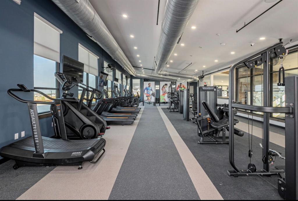 Fitness center featuring industrial-style exposed ductwork, recessed lighting, expansive windows with roller shades, and durable flooring