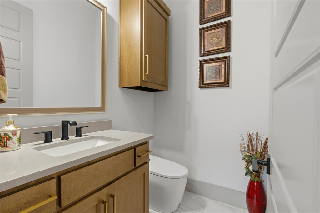 Wood-finish vanity cabinet with a stone-composite countertop, rectangular undermount sink, matte black widespread faucet, and wall-mounted storage cabinet