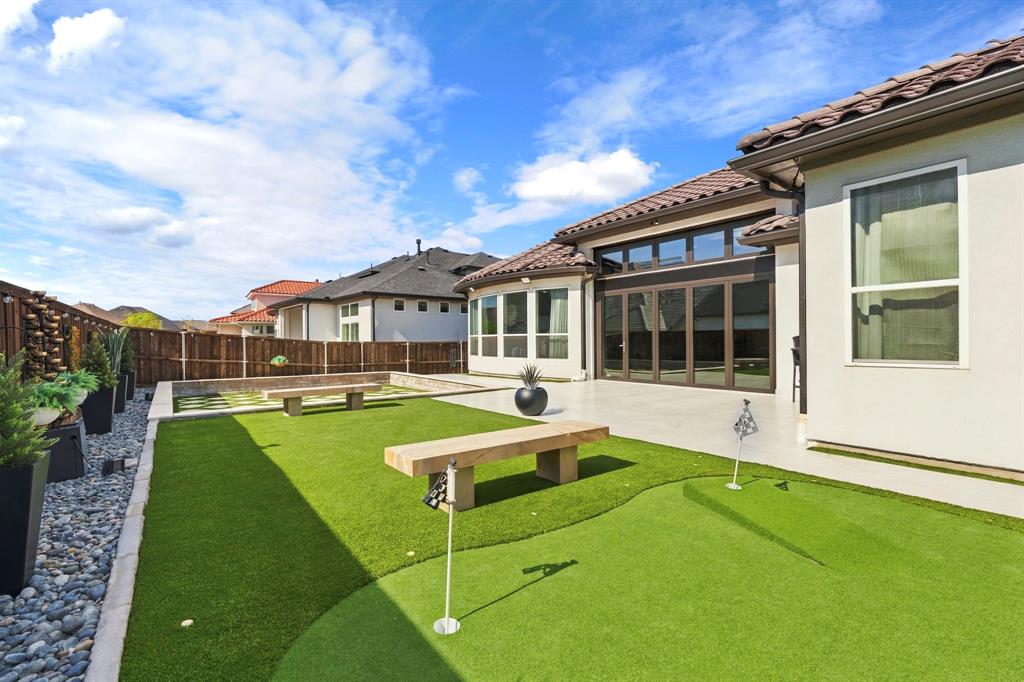 Backyard featuring a synthetic grass putting green, concrete patio, tile roof, multi-panel sliding glass doors, and perimeter wood fencing