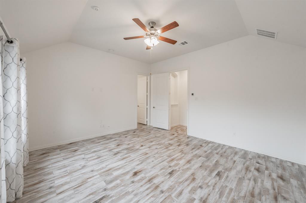 Spare room featuring vaulted ceiling, a ceiling fan, light wood-style floors, and baseboards
