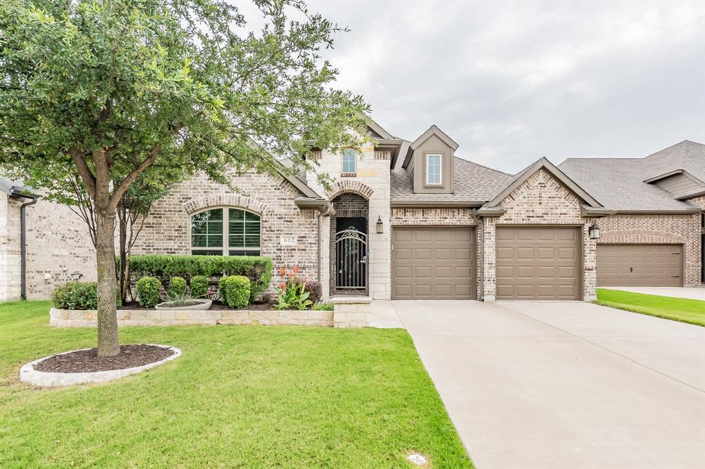 French country style house with brick siding, a front yard, driveway, roof with shingles, and an attached garage