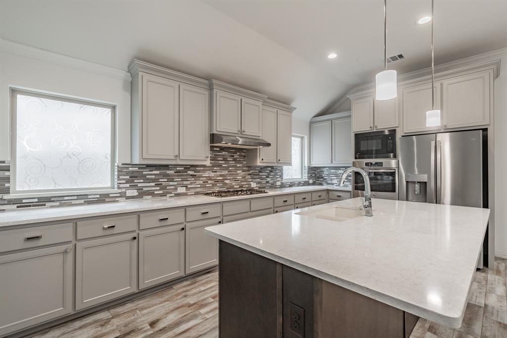 Kitchen with appliances with stainless steel finishes, light wood finished floors, gray cabinets, a sink, and vaulted ceiling
