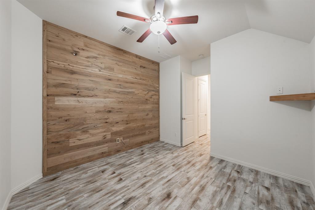 Spare room featuring wood walls, ceiling fan, wood finished floors, baseboards, and vaulted ceiling