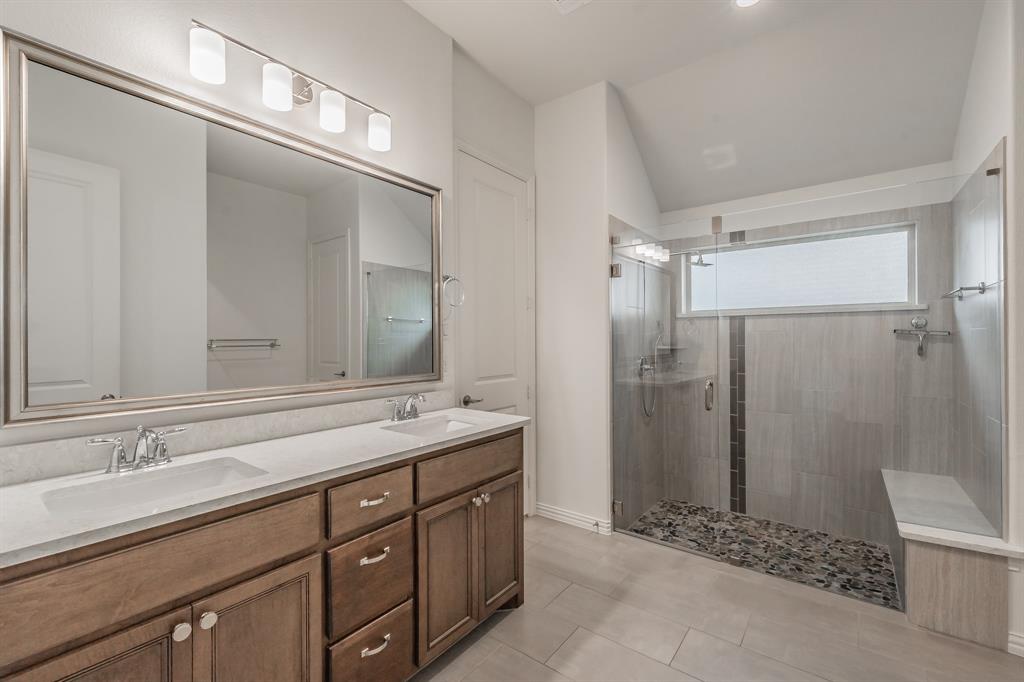 Bathroom featuring a stall shower, double vanity, tile patterned flooring, and vaulted ceiling