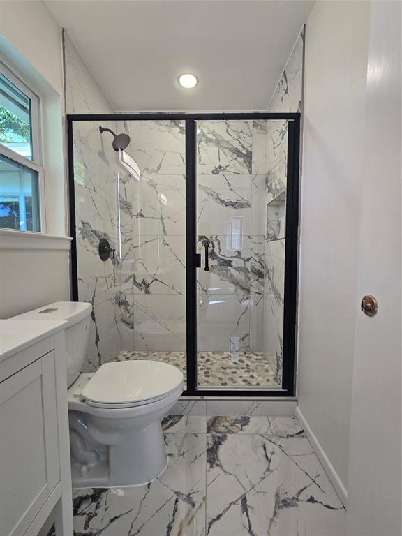 Walk-in shower featuring large-format patterned wall tile, black metal frame, integrated recessed niche, and pebble-tile flooring, complemented by a white vanity and matching large-format floor tile