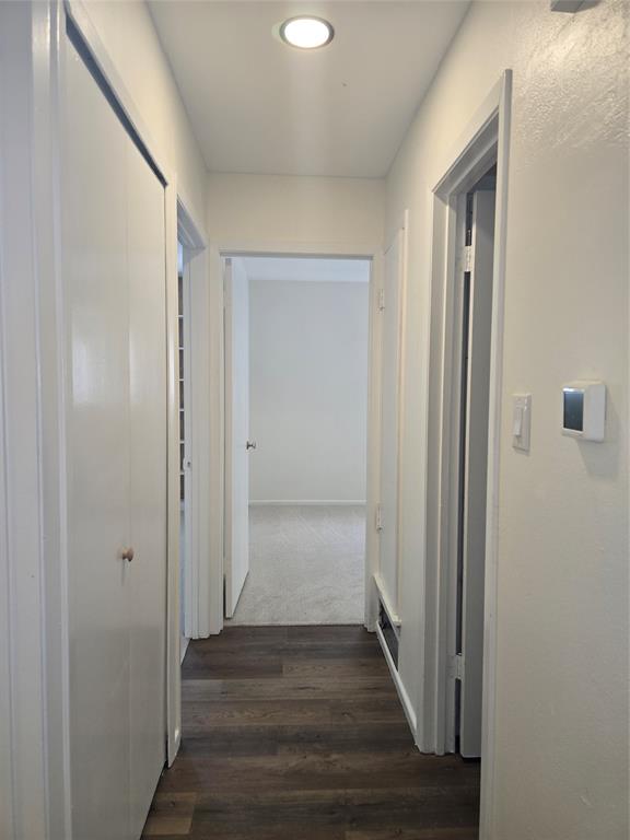 Hallway featuring wood-finish flooring, recessed ceiling lighting, a built-in closet with double-panel doors, and a wall-mounted thermostat