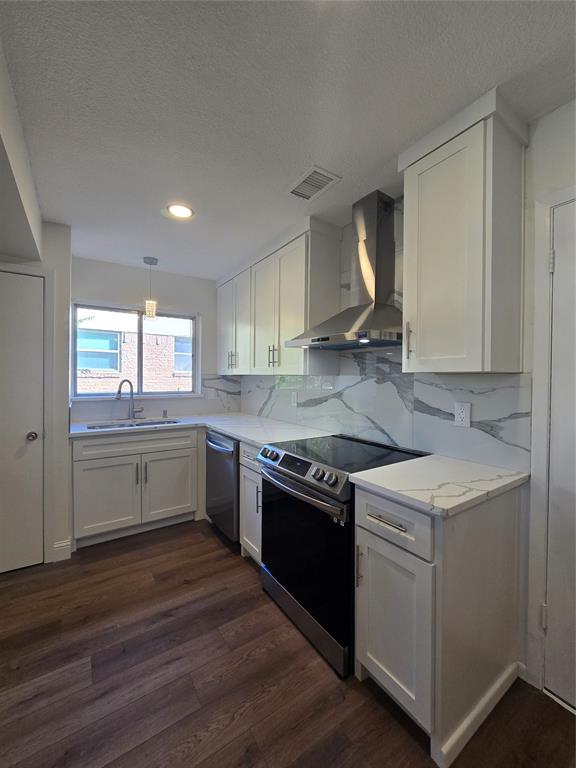 Kitchen featuring white shaker-style cabinetry, stone-patterned countertops, a full-height stone-patterned backsplash, stainless steel range with overhead chimney hood, and wood-finish flooring