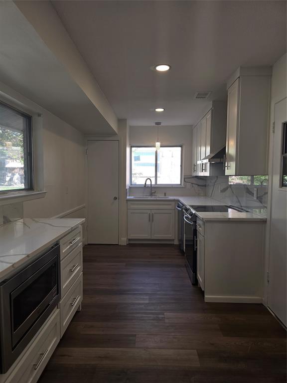 Kitchen featuring white shaker-style cabinetry, stone-patterned countertops, a full-height backsplash, stainless steel appliances, and dark wood-finish flooring