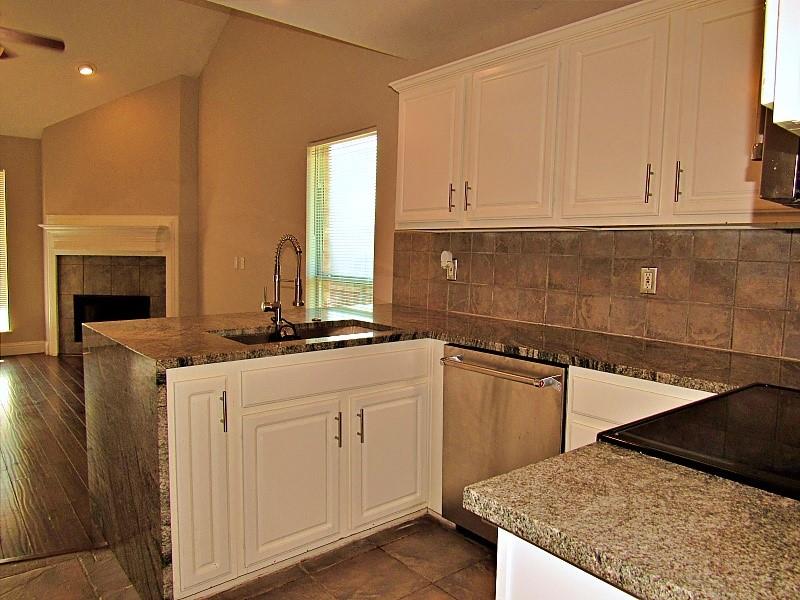 Kitchen featuring white shaker-style cabinetry, stone countertops with waterfall edge, stainless steel dishwasher, square tile backsplash, and a high-arch kitchen faucet