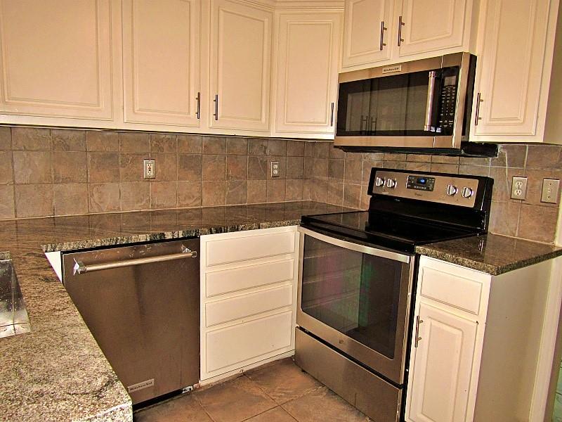 Kitchen featuring white shaker-style cabinetry, stone countertops, stainless steel appliances, and a tiled backsplash