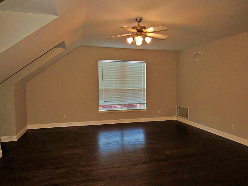 Vaulted ceiling featuring dark wood-finish flooring, a central ceiling fan with multi-bulb lighting, and a window with integrated blinds