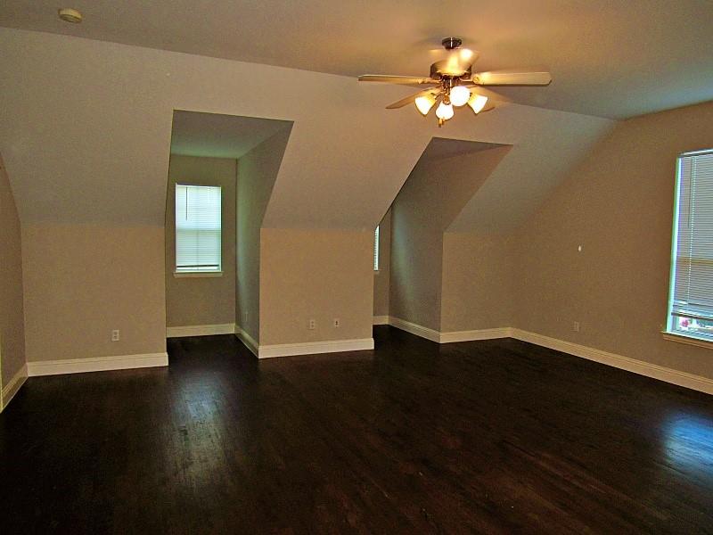 Open-concept room featuring vaulted ceilings, dark wood-finish flooring, two deep dormer alcoves, and a central ceiling fan with multi-light fixture