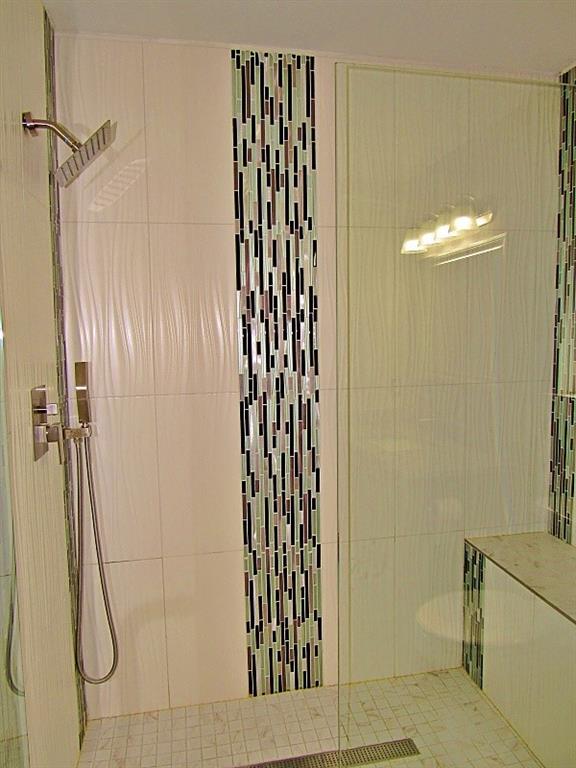 Walk-in shower featuring textured wall tile, a glass partition, a built-in tiled bench, mosaic accent banding, and a stainless steel rainfall shower head with a detachable handheld sprayer
