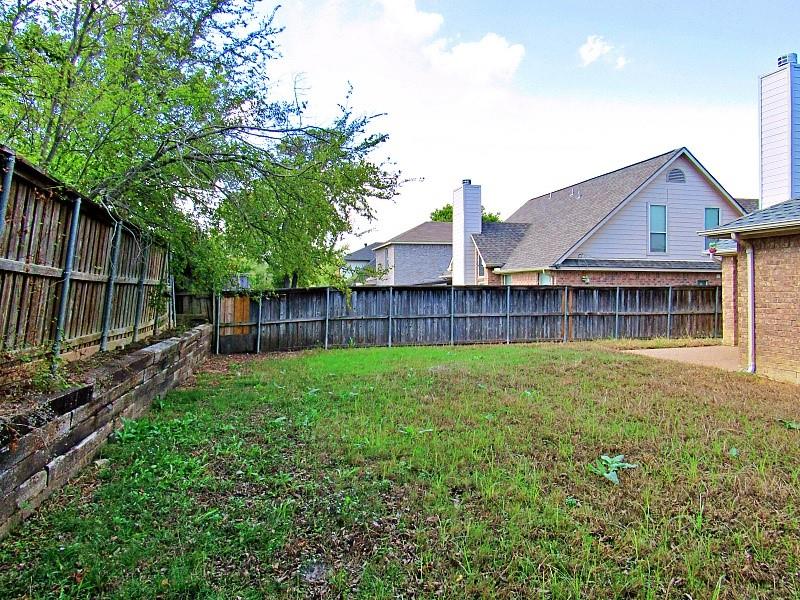Rear yard featuring timber retaining walls, wood fencing, and a concrete patio