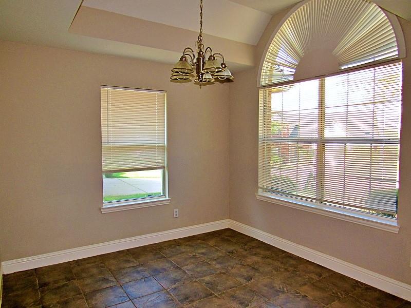 Tray ceiling with a multi-arm chandelier, large arched window, and ceramic tile flooring
