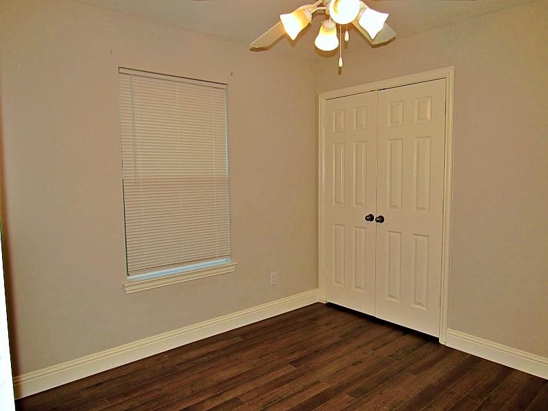 Neutral-toned interior featuring wood-finish flooring, a single-hung window with built-in blinds, double-panel closet doors, and a multi-light ceiling fixture