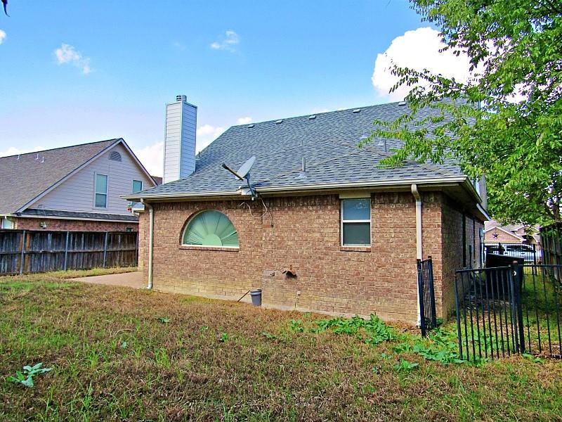 Brick exterior featuring a tall chimney stack, arched window, asphalt shingle roof, and metal perimeter fencing