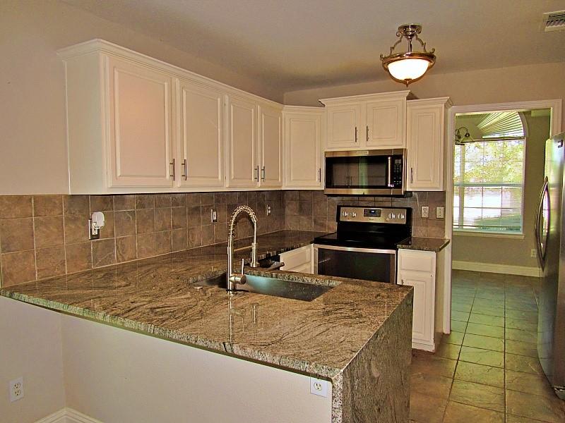 Kitchen featuring white cabinetry, stone countertops, square tile backsplash, stainless steel appliances, and a high-arch faucet