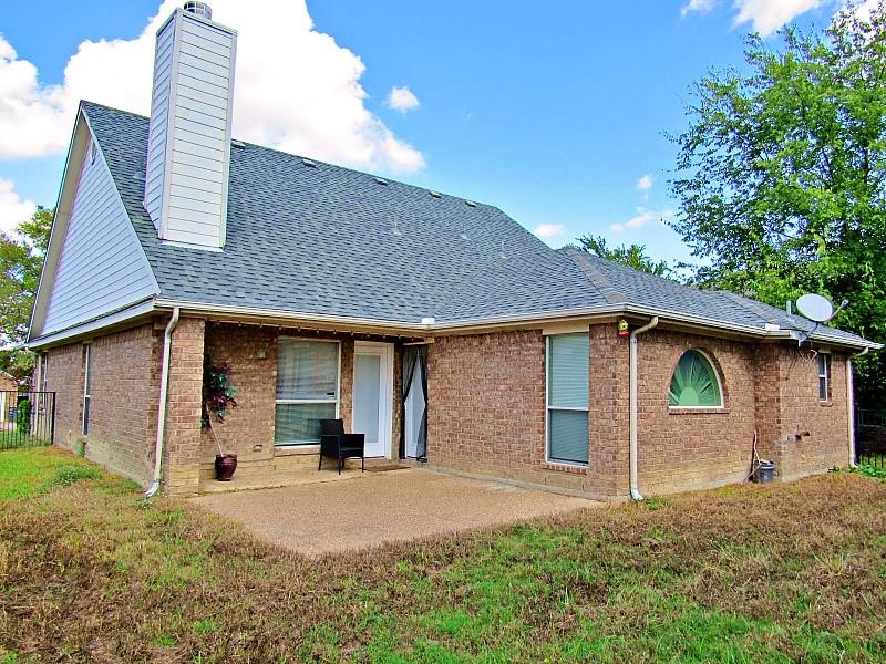 Brick exterior featuring a concrete patio, a tall chimney, and a decorative arched window