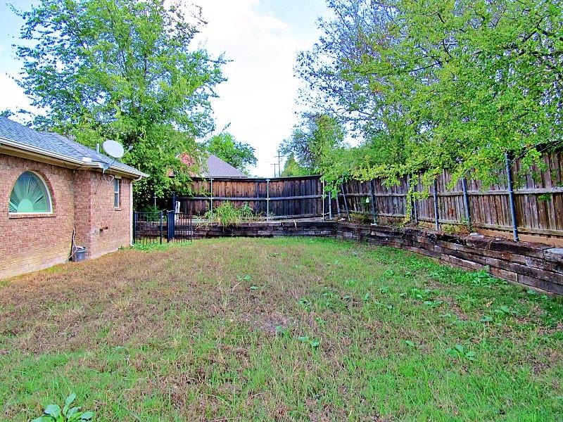 Backyard featuring a brick exterior wall, arched window, wood-paneled privacy fencing, and tiered landscape retaining walls